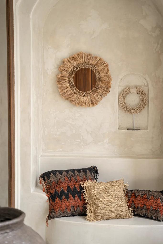 Boho spiegel Mowgli op een sfeervolle zandkleurige muur, met handgemaakte kussens die een warme, gezellige sfeer creëren.