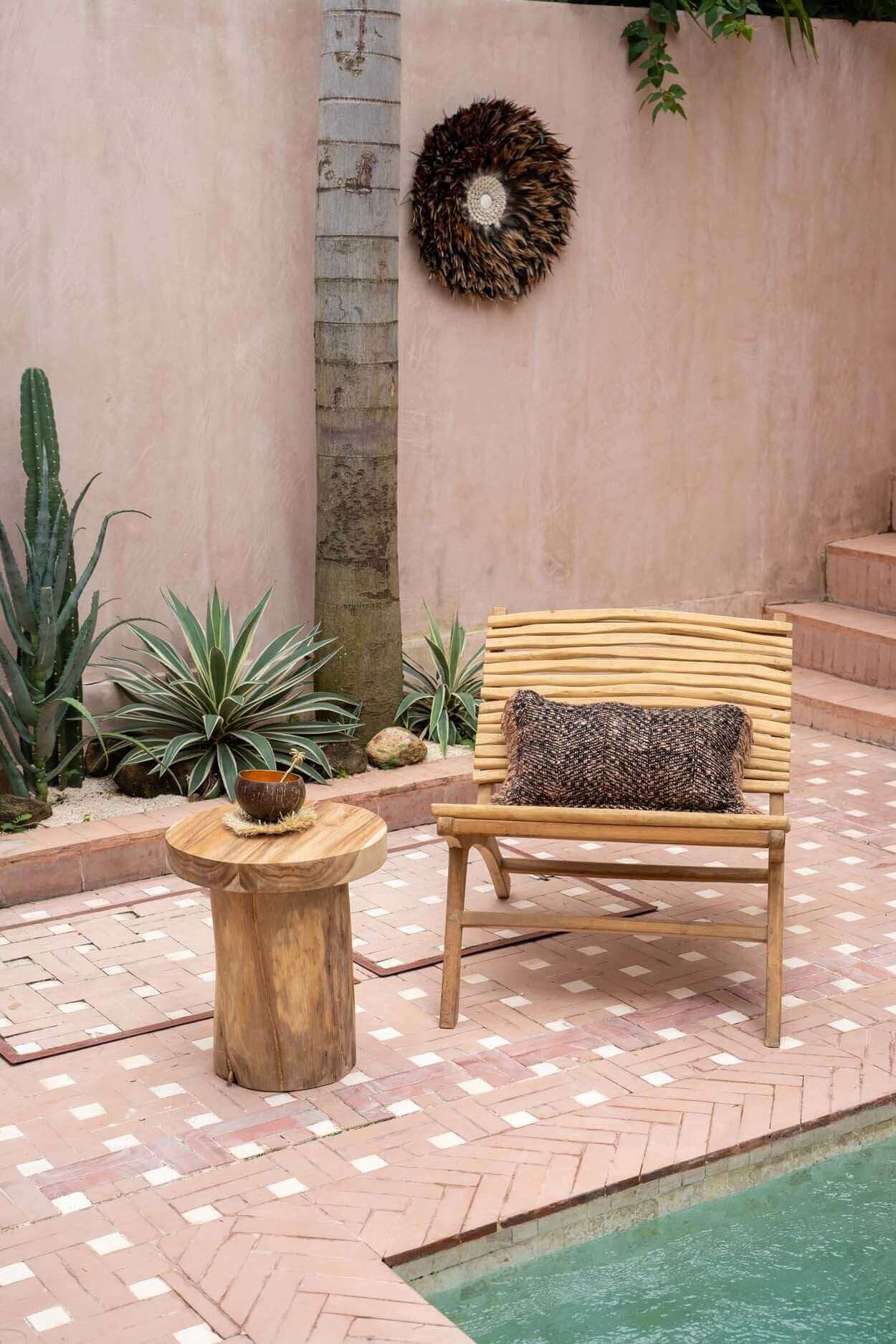 Boho stoel de Islander, handgemaakt van teakhout, naast een zwembad in een zonnige tuin, omringd door cactussen en groene planten.