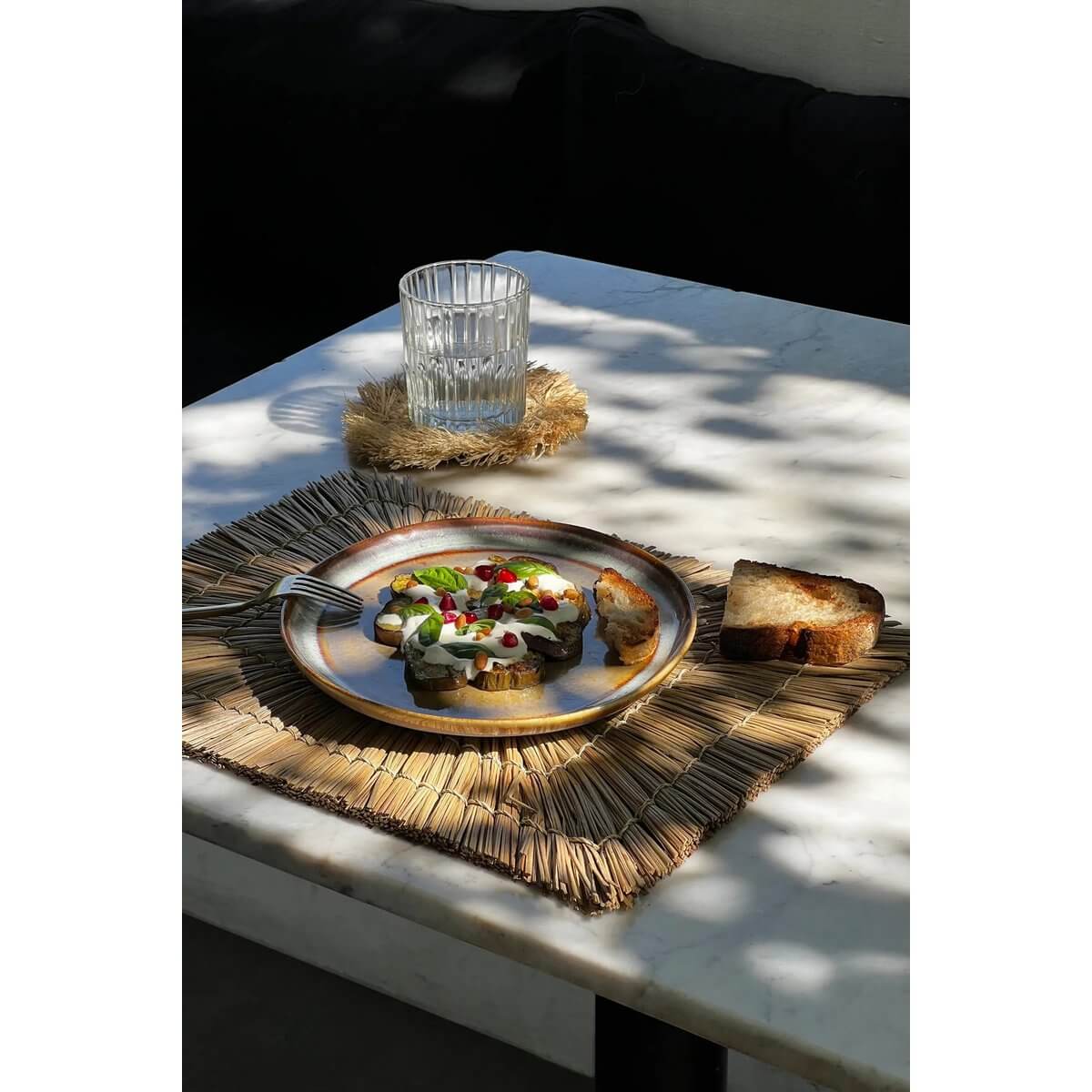 Bohemian style table setting with De Alang Alang rectangular placemat in neutral tones, featuring a plate of food and glass on a sunny patio.