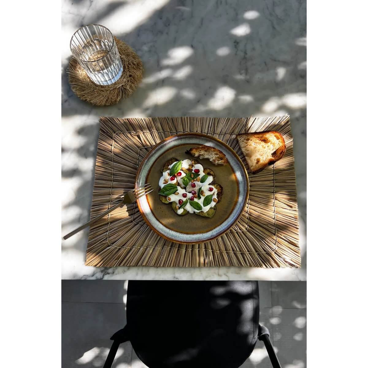 De Alang Alang Bohemian placemat with natural tones, enhancing a rustic table setting with delicious dish and bread.