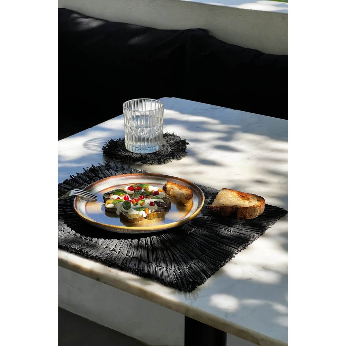 Bohemian black rectangular placemat on table with plate of food and glass, showcasing De Alang Alang design in a chic setup.