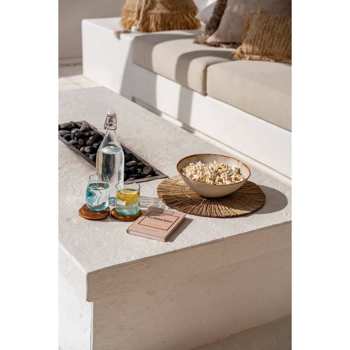Chic bohemian table setting with a Bazar Bizar Living round placemat, drinks, snacks, and a book in a stylish outdoor area.