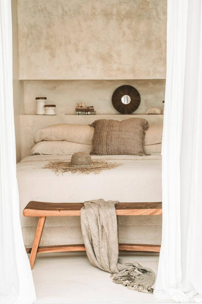 Strandhoed van zeegras met bandana op bed in rustieke slaapkamer, omgeven door natuurlijke elementen en rustige inrichting.