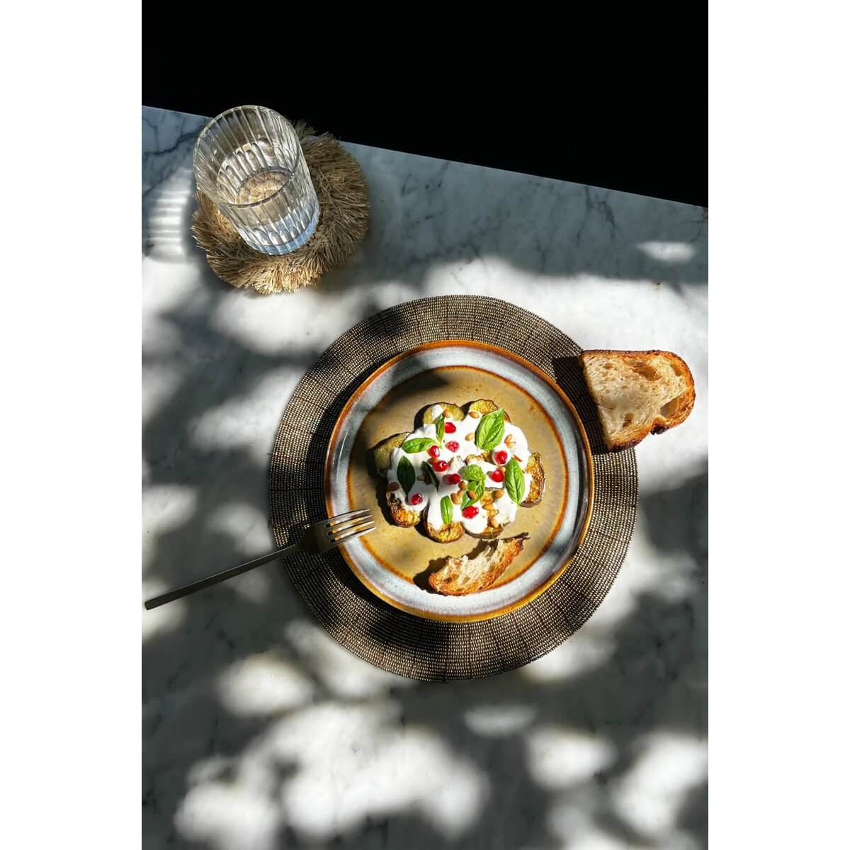 Breakfast dish on Bohemian beaded placemat with toast and water, surrounded by sunlit patterns.
