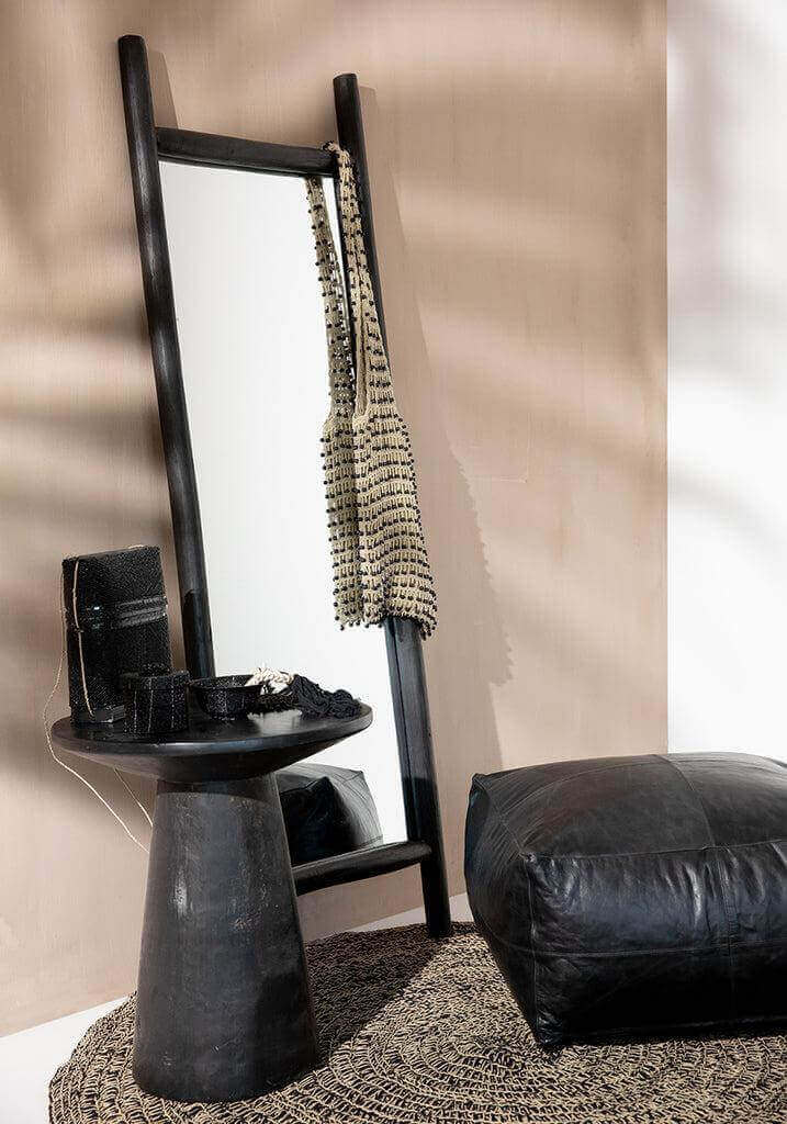 Stijlvol interieur met grote spiegel, zwarte poef en decoratief tafeltje met kralen en accessoires.