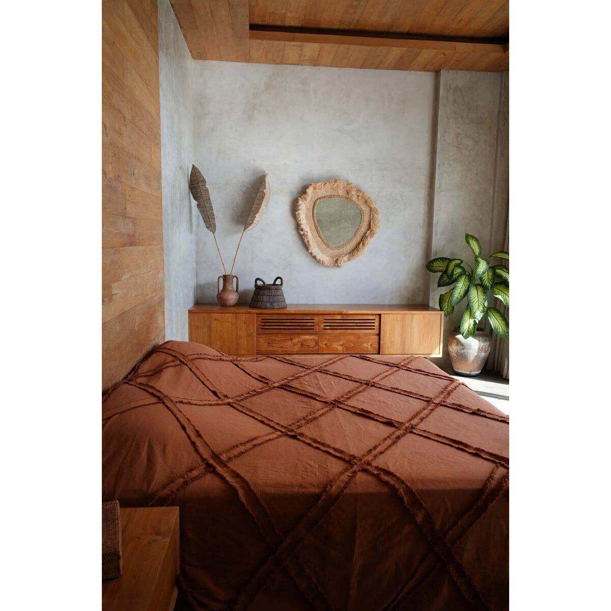 Stijlvolle terracottakleurige Berber-bedsprei in een rustieke kamer met houten meubels en een decoratieve spiegel.
