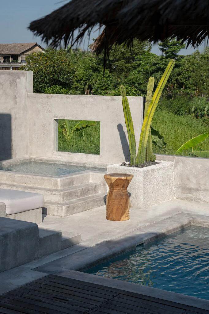 De Bloom Kruk in een serene tuin naast een zwembad, gemaakt van duurzaam suarhout met donkere natuurlijke tinten en geometrische vorm.