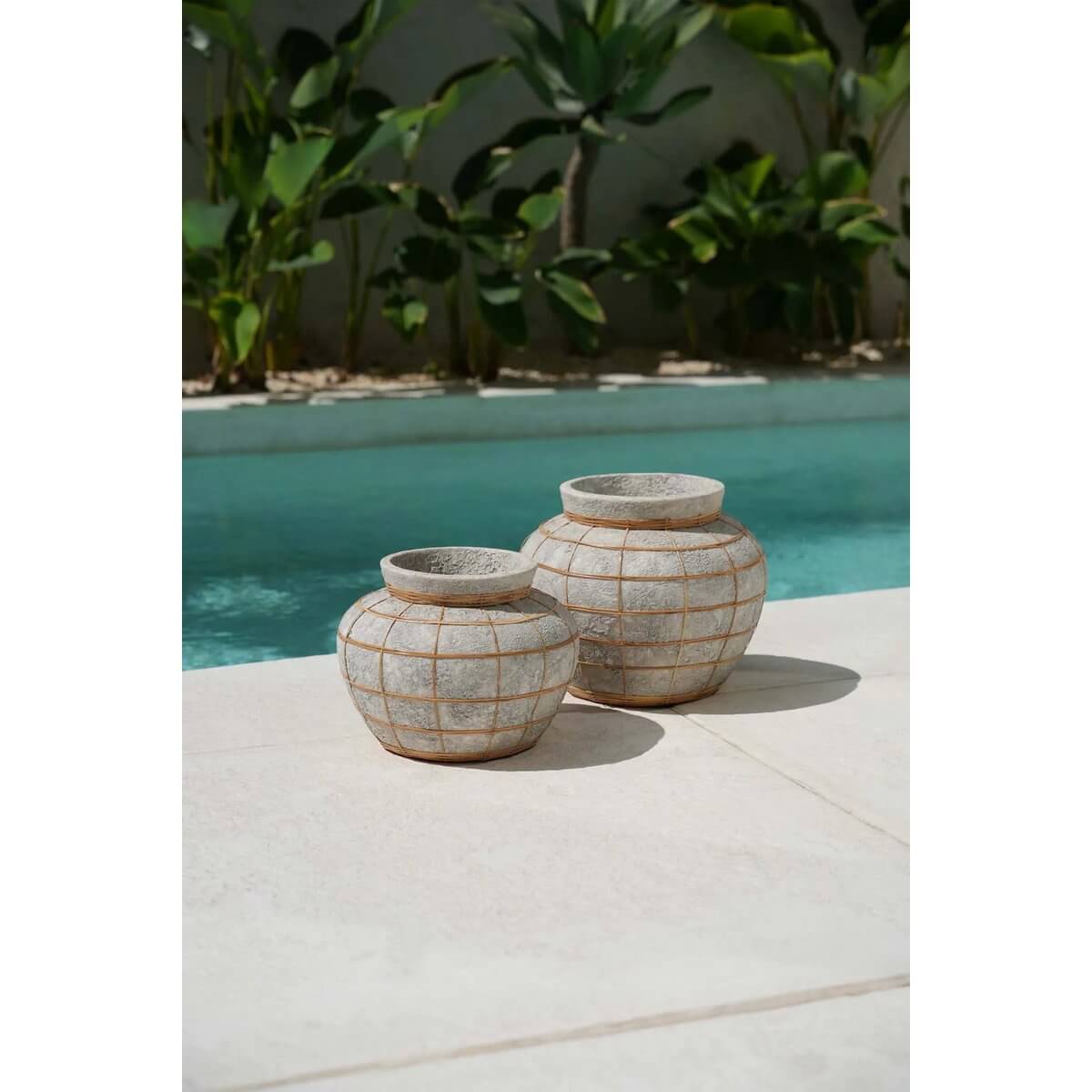 Twee terracotta buikvazen met rotandetails, geplaatst naast een zwembad op een zonnige dag.