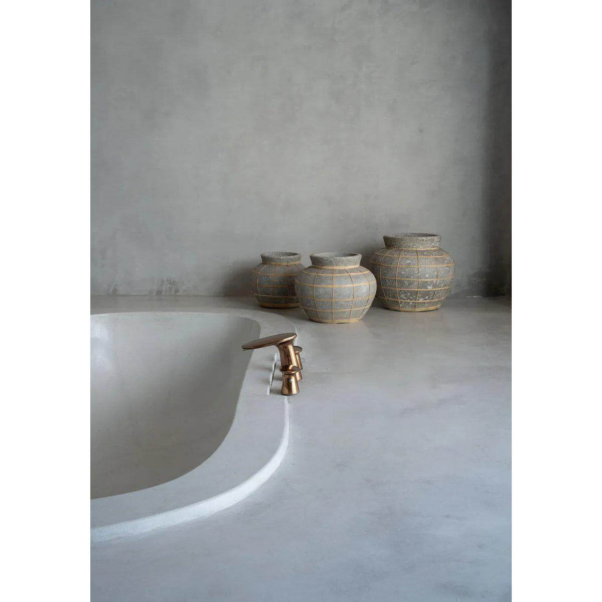 Stijlvolle badkamer met terracotta vazen en moderne kraan naast betonnen wand.