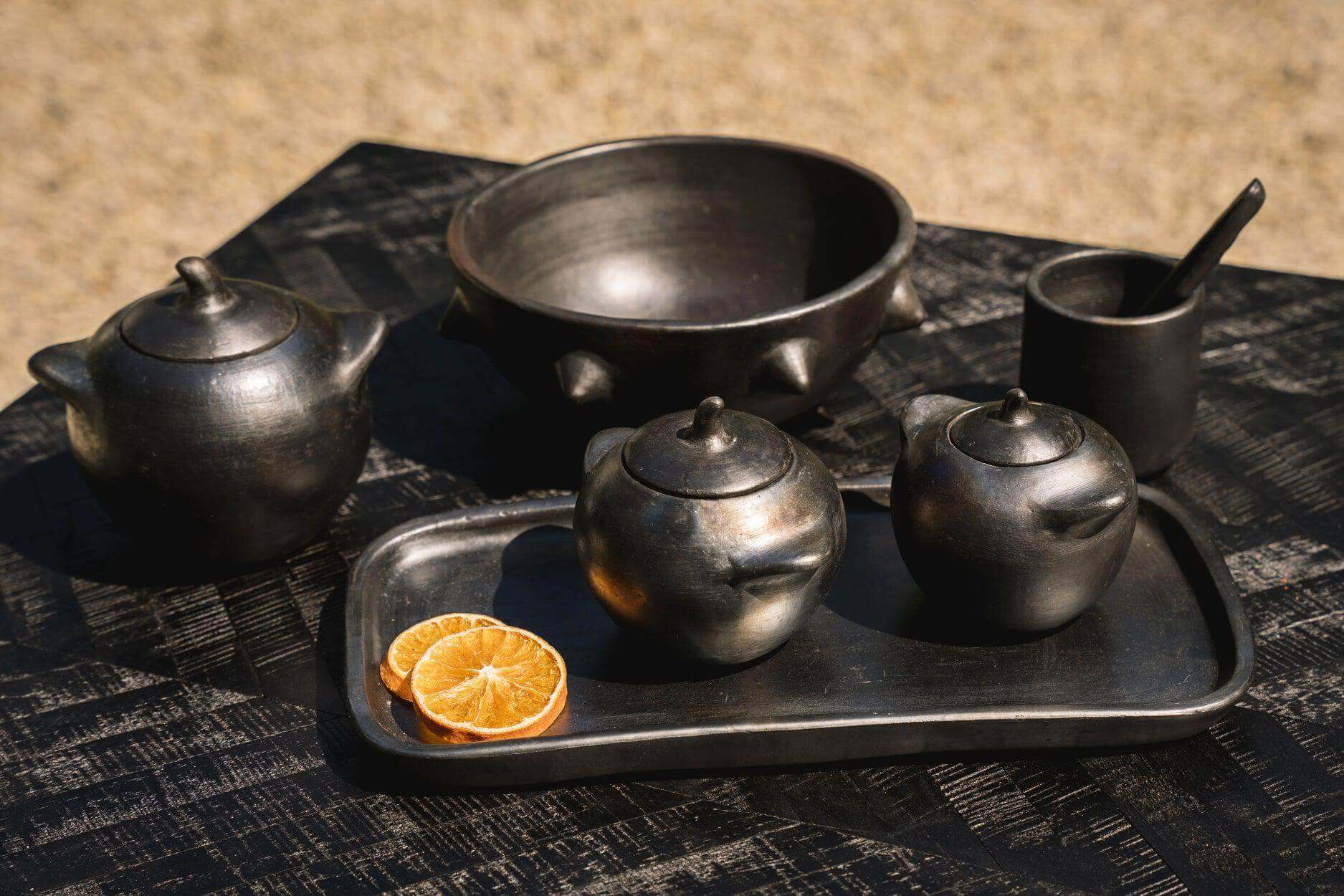 Zwart-gebrande serviescollectie op tafel met citrus accents voor een unieke uitstraling. Perfect voor kleurrijke maaltijden en stijlvolle presentatie.