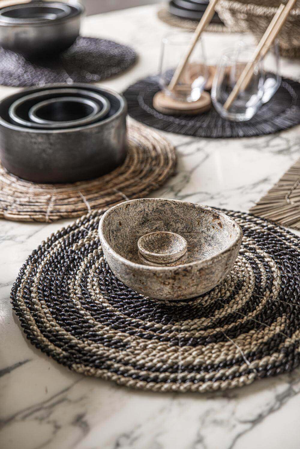 Tafeldecoratie met gebrande terracotta kommen in zwart, set van 3, op een prachtig geweven placemat op een marmeren tafel.