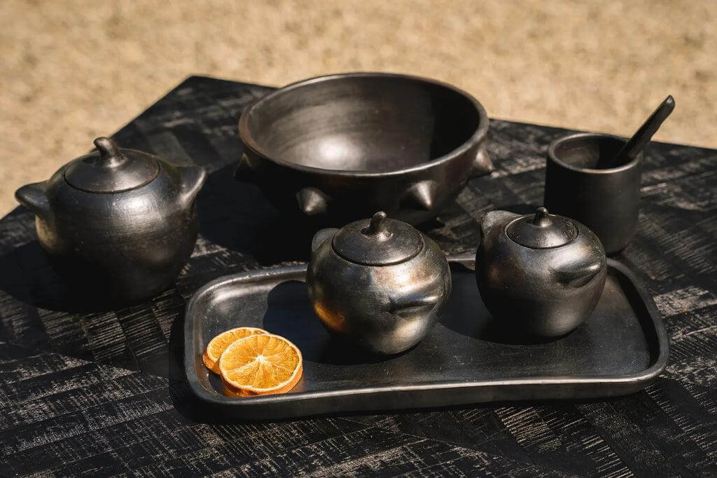 Zwarte teakhouten schaal en servies op tafel met sinaasappelschijfjes, perfect voor badkamers of snacks.
