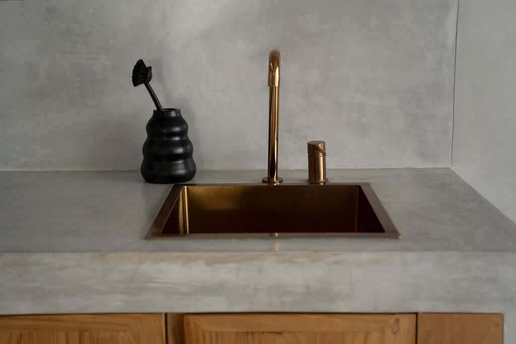 Zwarte De Burned Vaas naast gouden keukenkraan op betonblad, ideaal voor bloemen of keukengerei. Voeg stijl toe aan je keuken!