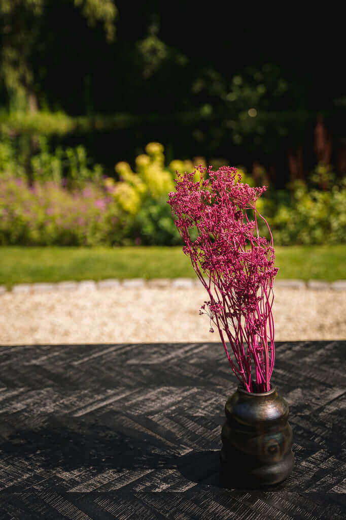 Zwart gebrande vaas met roze gedroogde bloemen op een tafel in de tuin, perfect voor keuken of tafeldecoratie.