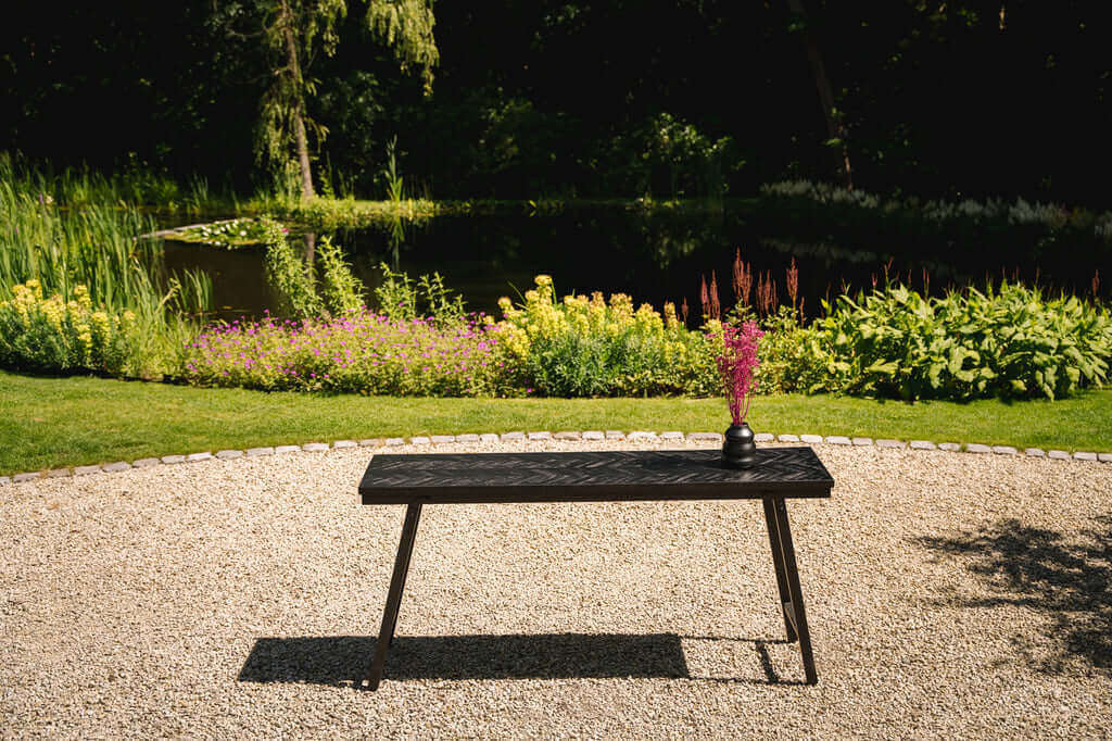 Tuin met een elegante zwarte eettafel en een vaas met bloemen, omgeven door groene natuur en kleurrijke bloemen.