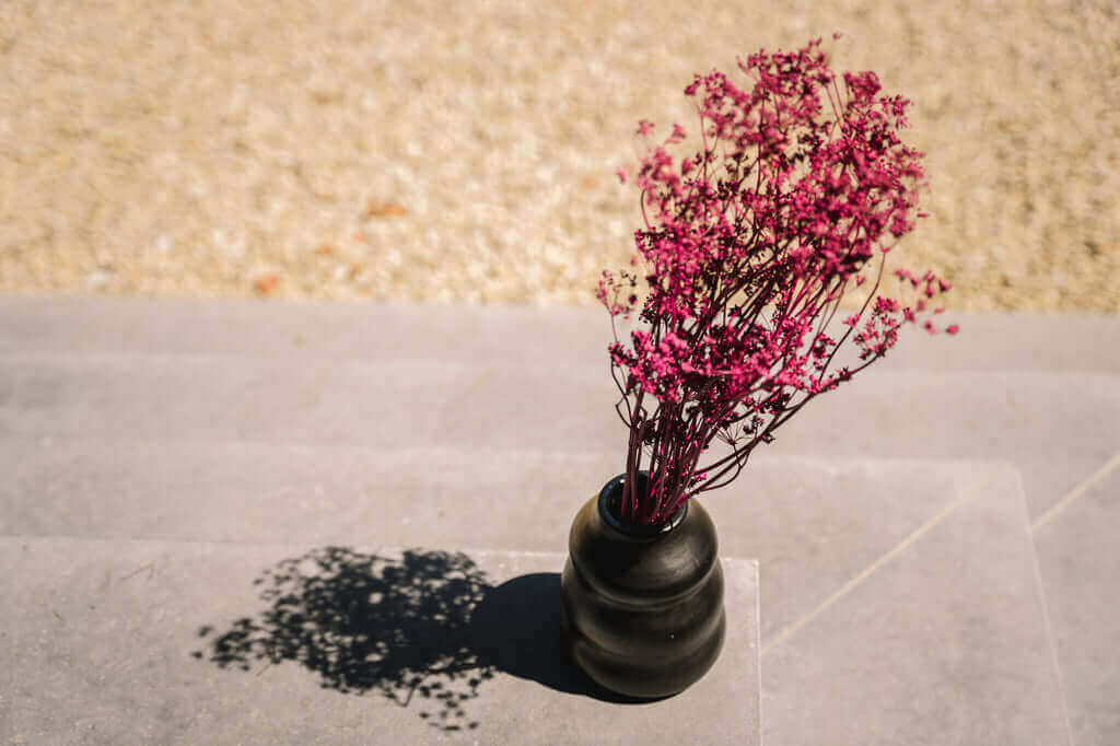 Zwarte gebrande vaas met roze gedroogde bloemen op stenen trap, ideaal voor keuken of tafel. Voeg een stijlvolle touch toe aan je interieur.