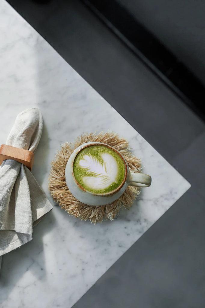Marmeren tafel met een De Cascais Koffiemok L gevuld met groene thee-latte, naast linnen servet, perfect voor een stijlvol ontbijt.
