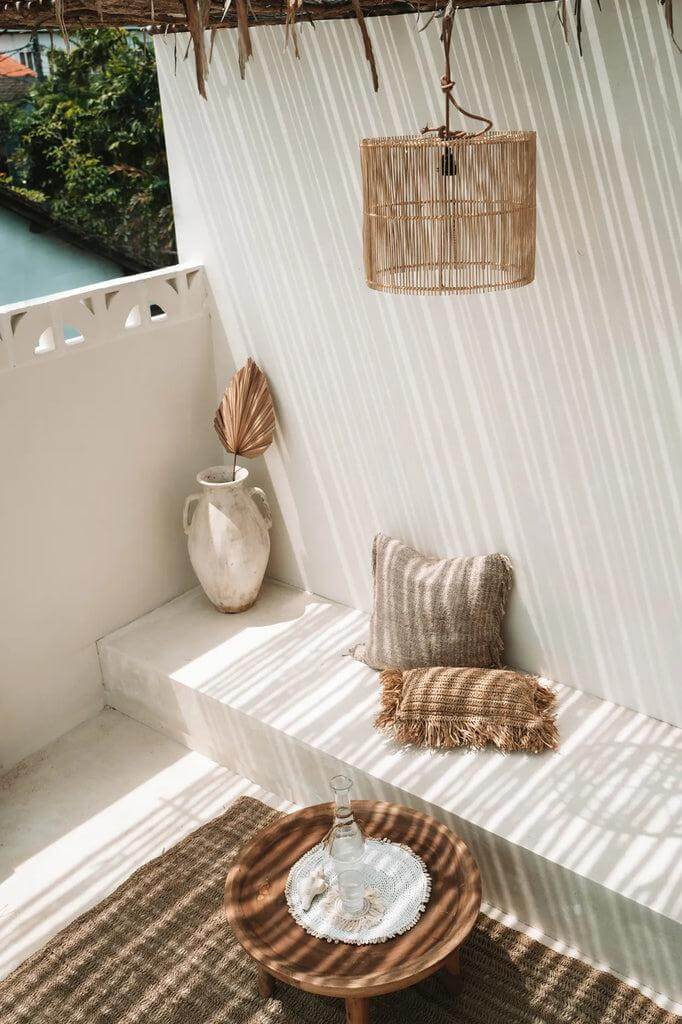 Stijlvolle rotan hanglamp verlicht moderne buitenruimte met kussens en pot. Perfect voor elegante en natuurlijke sfeer.