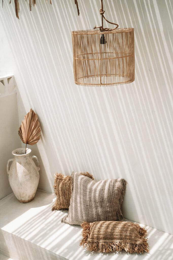 Stijlvolle rotan hanglamp die prachtige schaduwen werpt in een serene ruimte met natuurlijke elementen en kussens.