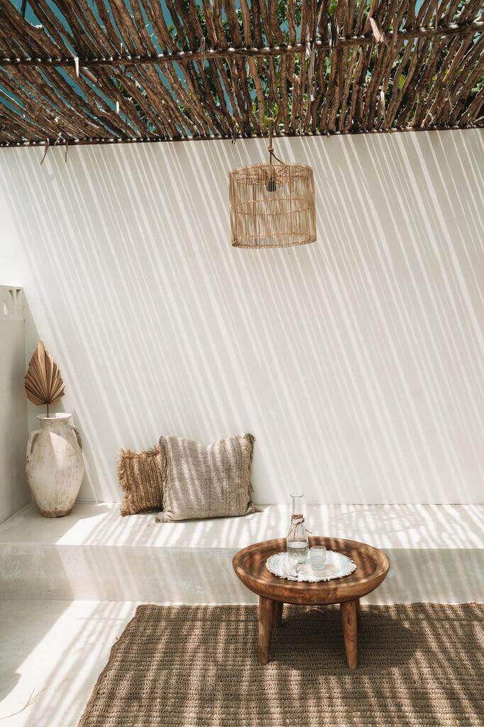 Stijlvolle rotan hanglamp De Chacha Naturel werpt schaduwen op moderne zithoek met houten tafel en kussen in zonnige ruimte.
