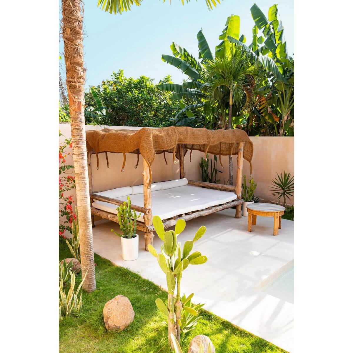Bohemian-style lounging area with natural coco shade in lush tropical garden, featuring wooden daybed, ideal for relaxation.