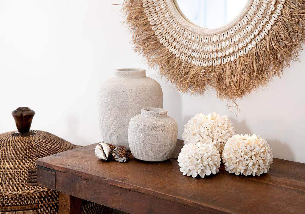 Decoratief interieur met handgeweven rotan mand, beige vazen en een schelpen spiegel op een houten tafel.