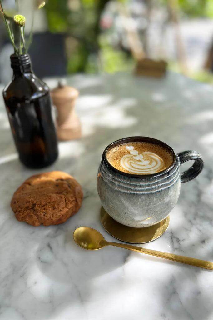 Espresso in een De Comporta keramische mok naast een versgebakken koekje op een marmeren tafel.