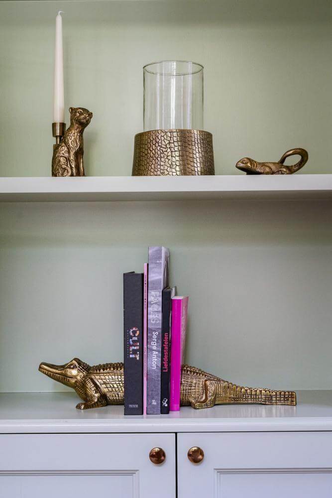 Alt Tag: De Croco kaarsenhouder in messing op een plank, gecombineerd met decoratieve boekensteunen. Stijlvol en eigentijds design.