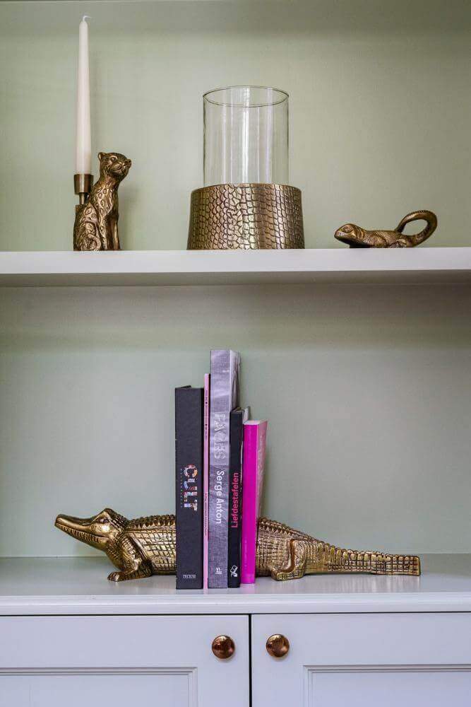 Alt Tag: De Croco kaarsenhouder in messing op een plank, gecombineerd met decoratieve boekensteunen. Stijlvol en eigentijds design.
