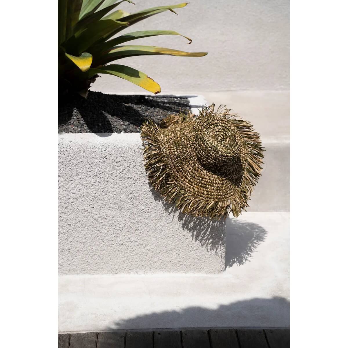 De Fiesta-hoed van raffia in junglegroen tinten, liggend op een betonnen muurtje in de zon.
