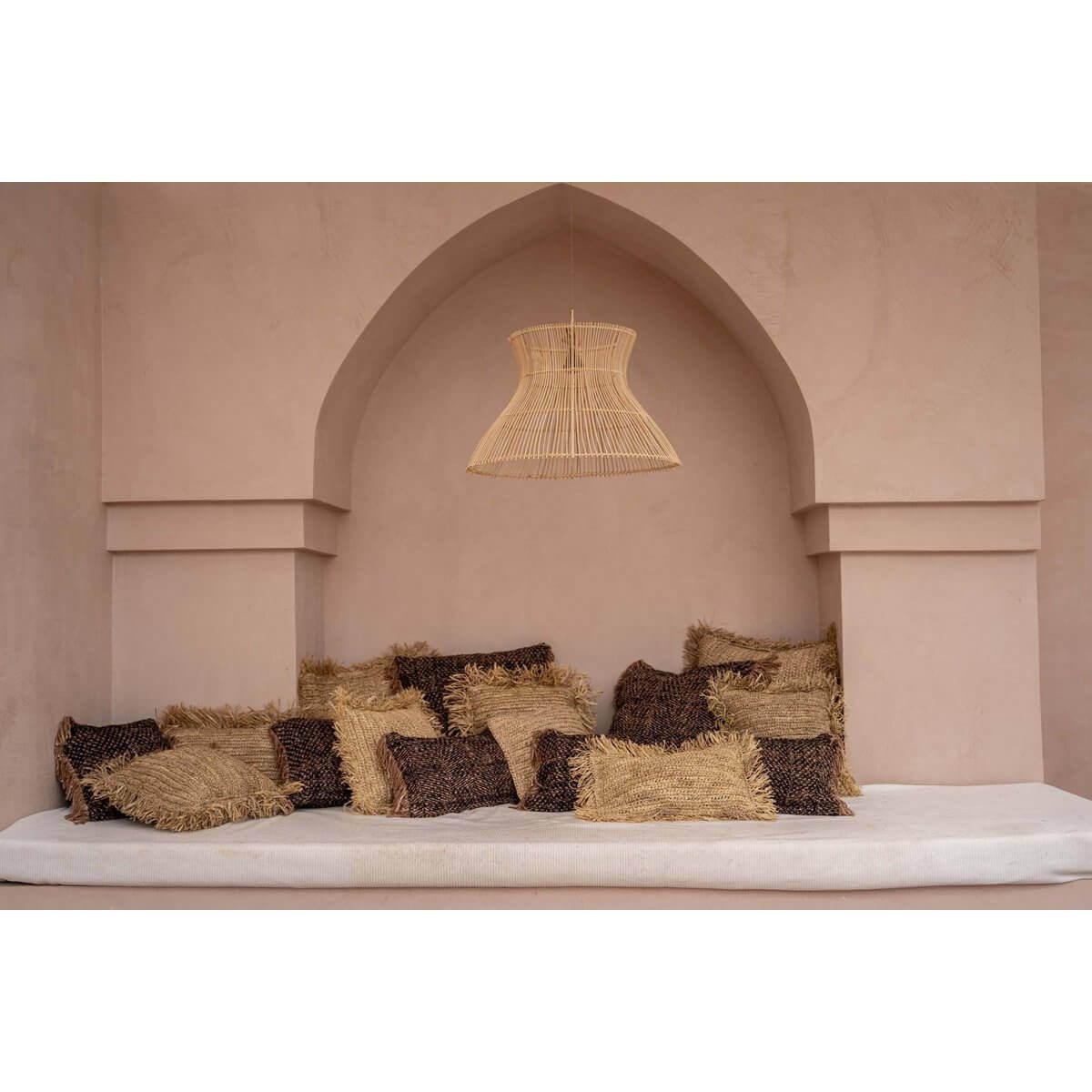 Kegelvormige rotan hanglamp boven bank met kussens, creëert elegante schaduwen. Geschikt voor binnen of overdekte buitenruimtes.