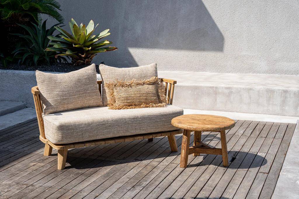 Rustieke teakhouten salontafel naast moderne outdoor bank op houten terras.