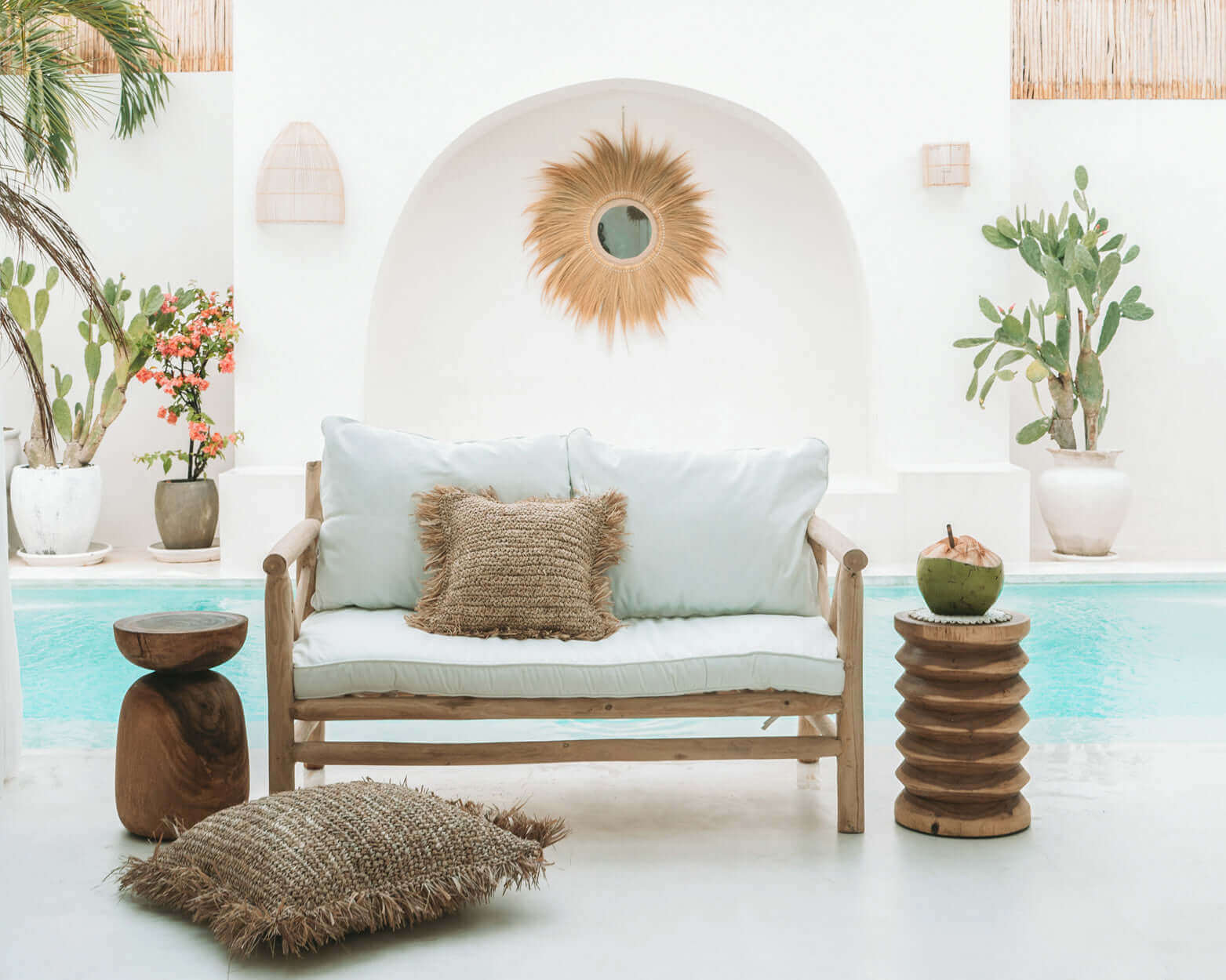 Stijlvolle zomerse patio met houten kruk, bank en decoratieve kussens bij zwembad. Perfect voor ontspannen in natuurlijke sfeer.