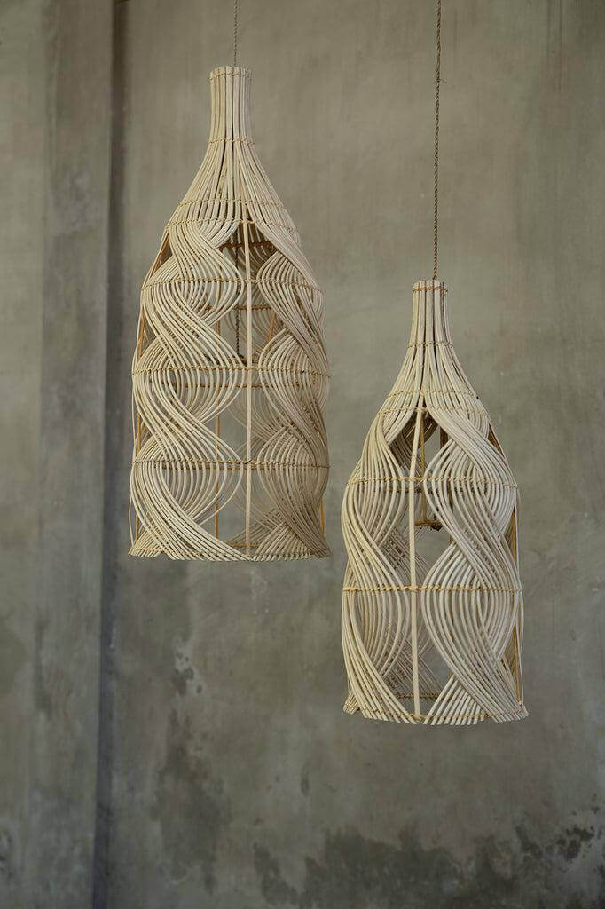 Twee De Garaffa rotan hanglampen in flesvorm tegen een betonnen muur, veelzijdig als hanglamp, vloerlamp of tafellamp.