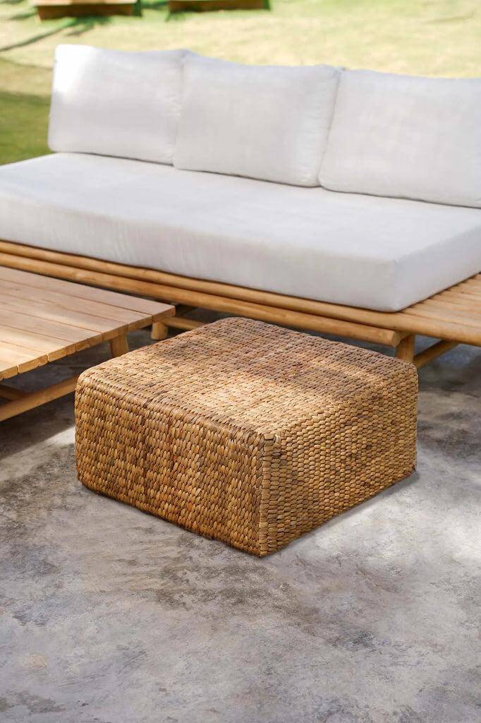 Vierkante waterhyacinten poef, naturel, naast een houten bank voor een natuurlijke interieurstijl.