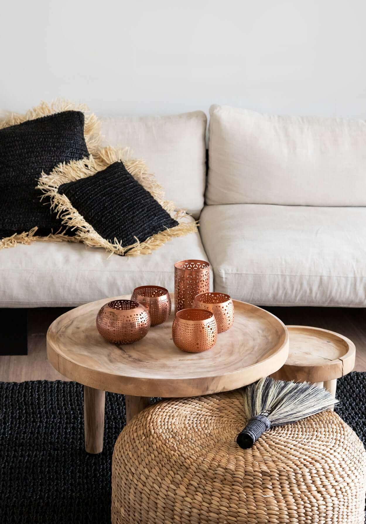 Boho interieur met handgemaakte Hyacinth Poef, houten bijzettafel en decoratieve koperkleurige theelichthouders op een zwarte tapijt.