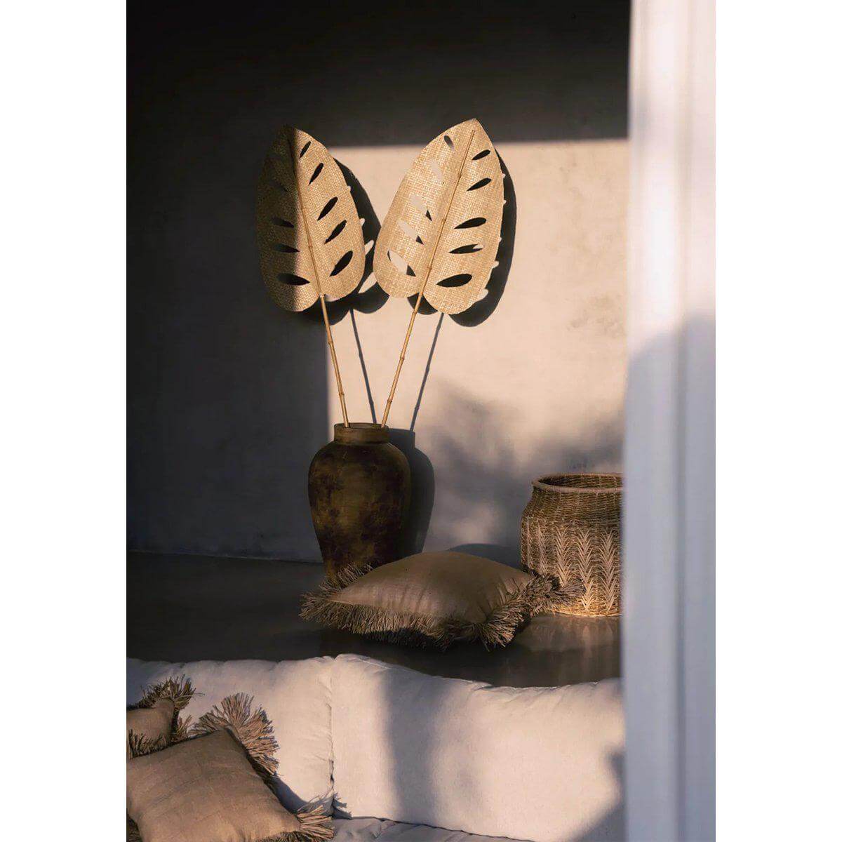 Gezellige woonkamer met naturelkleurige kussenhoes van jute en raffia, samen met decoratieve pot en bladeren voor een vakantiegevoel.