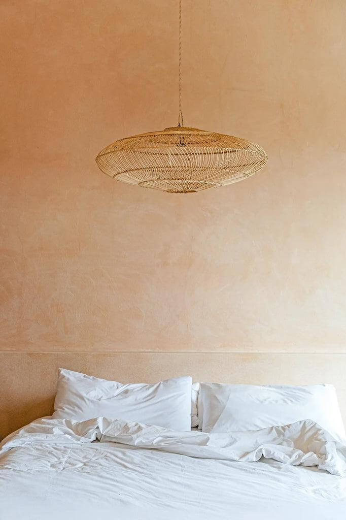 Stijlvolle De Macaron Hanglamp in naturel rotan, boven een knusse slaapkamer, brengt speelse elegantie en warme verlichting.