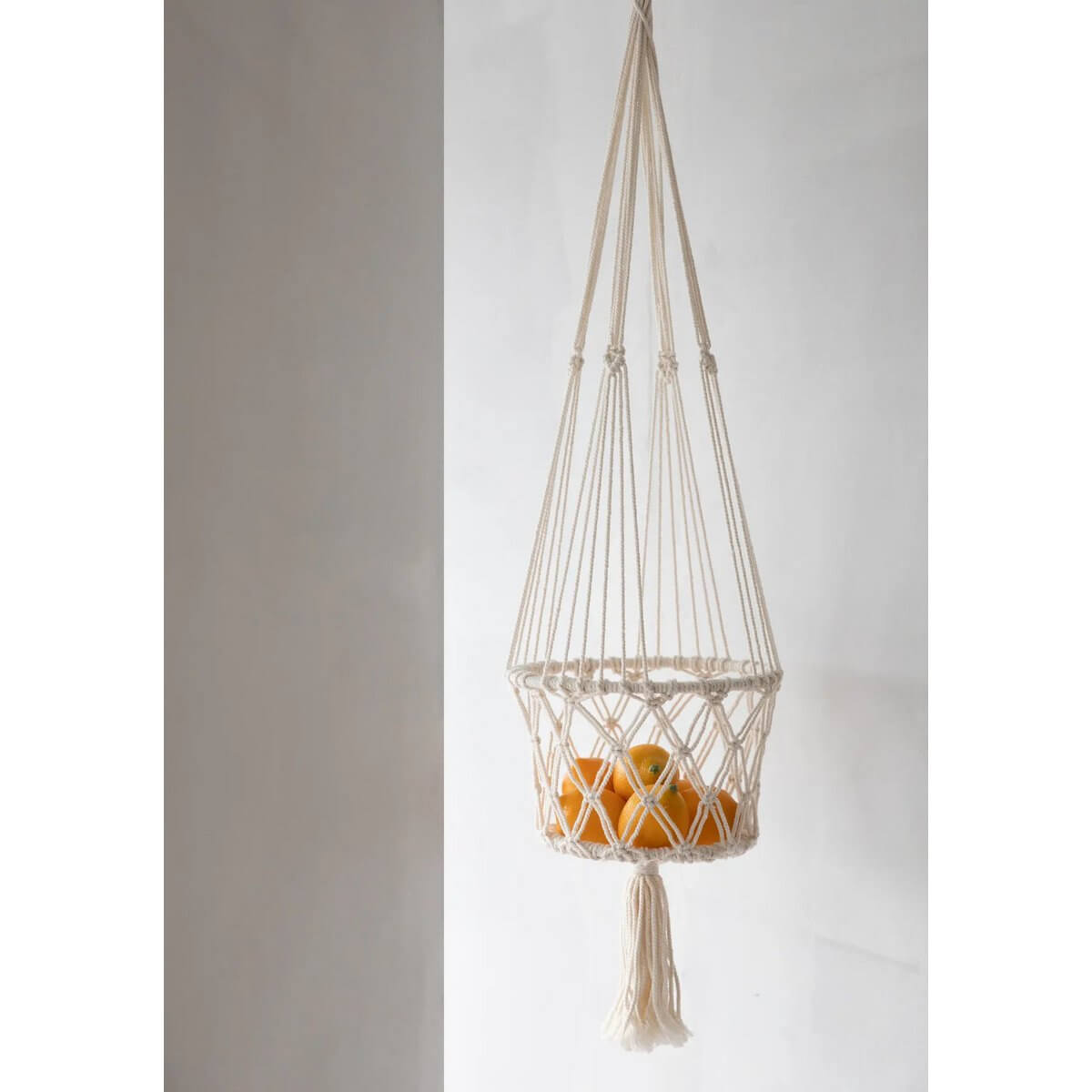 Bohemian macramé plant hanger in white with oranges inside, adding a decorative touch to indoor spaces. Perfect for natural or artificial plants.