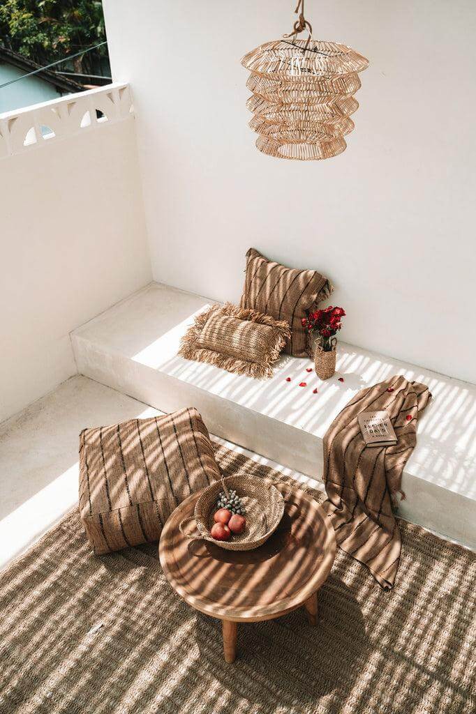 Boheemse stijl patio met rotan hanglamp, gevlochten kussens, en natuurlijke decoratie op houten tafel in de zon.