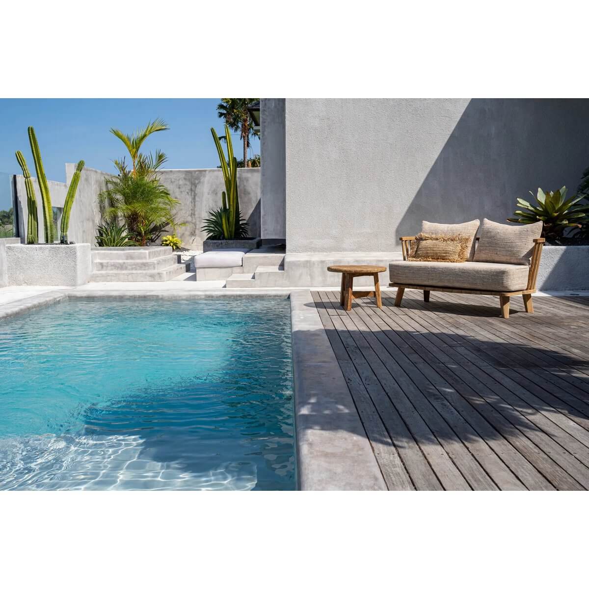 Bohemian-style De Malawi tweezitter in natural beige by a pool on a sunny day, showcasing comfort and style with recycled teak.
