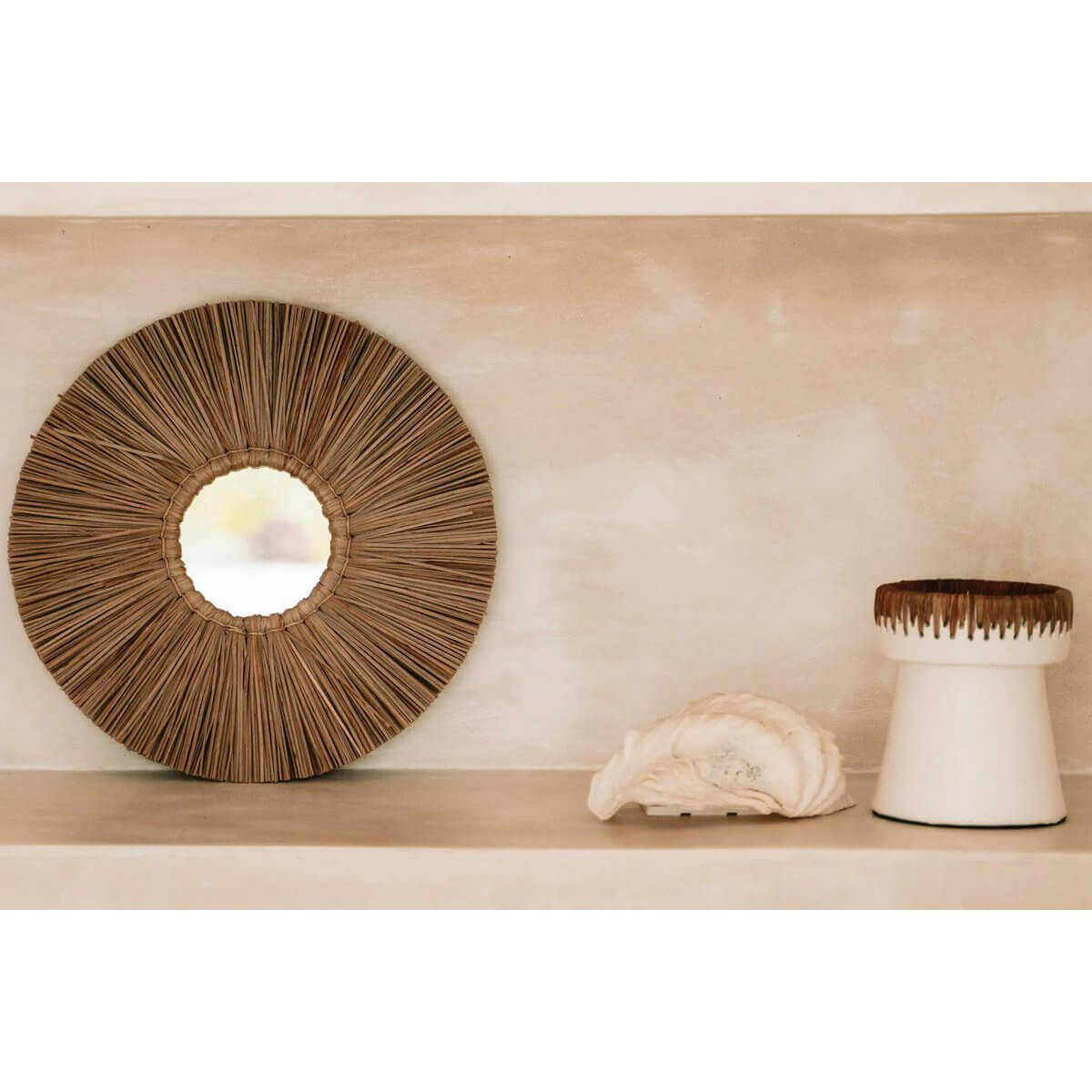 Ronde decoratieve raffia spiegel en witte terracotta kaarsenhouder op plank, stijlvol interieur design.