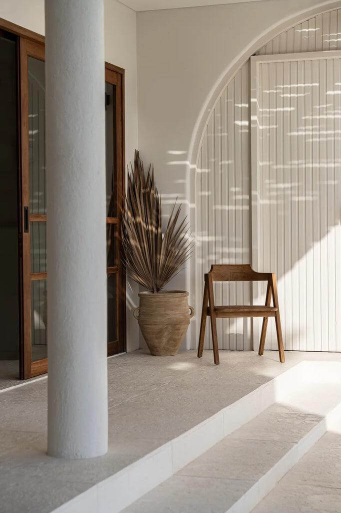 Elegant houten Nihi Sumba eetkamerstoel in stijlvolle buitenruimte, ideale mix van modern design en warme teaktinten.