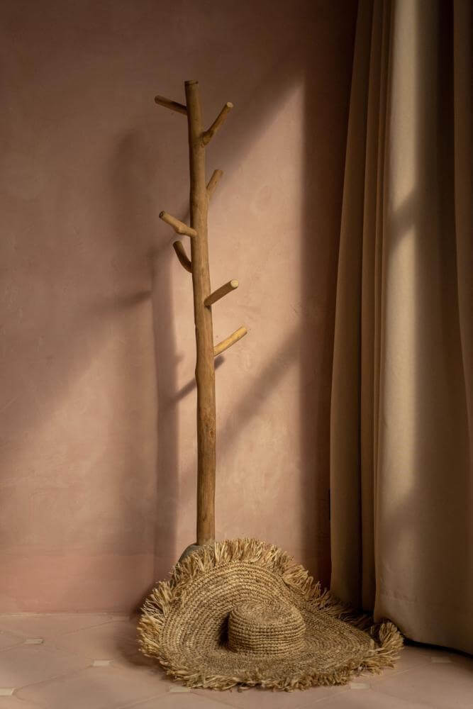 Alt Tag: Stijlvolle De Oceaan Hoed van raffia, perfect voor vakanties en festivals, ligt tegen een rustieke houten kapstok.