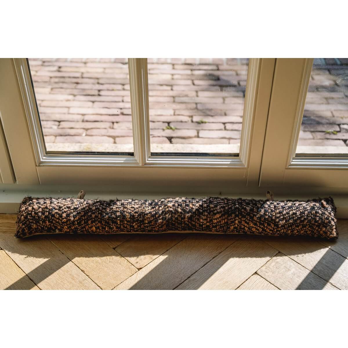 De Oh My Gee Deurstop - Stijlvolle zwarte koperen deurstopper voor isolatie, geplaatst onder raam op houten vloer.