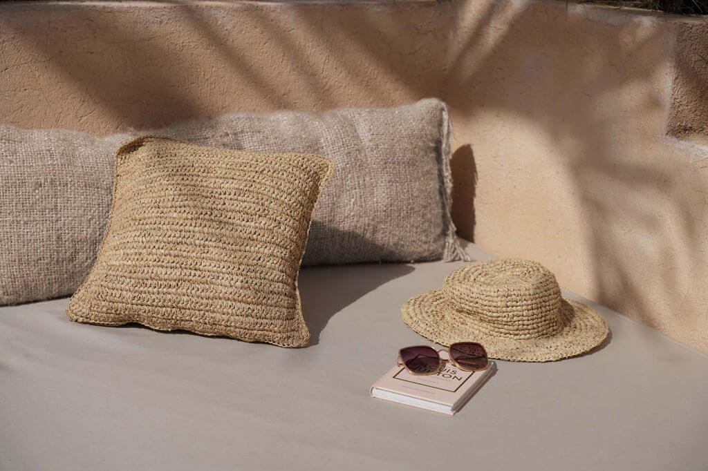 Gezellige zithoek met beige boho-kussen en rieten hoed, perfect voor een stijlvolle buitenruimte.