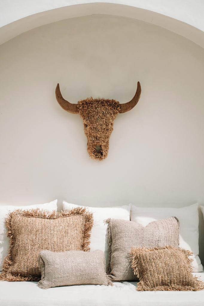 Alt Tag: Boho kussenhoezen in beige op een bank met een rustieke stierkop wanddecoratie, perfect voor een stijlvolle en chique interieurlook.