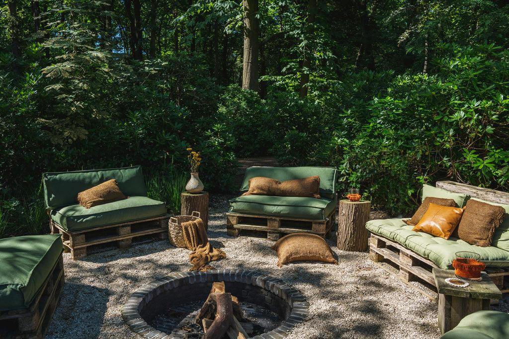 Rustieke boho tuin met groene en bruine palletbanken en kussenhoezen, omgeven door groen, ideaal voor ontspanning en gezelligheid.
