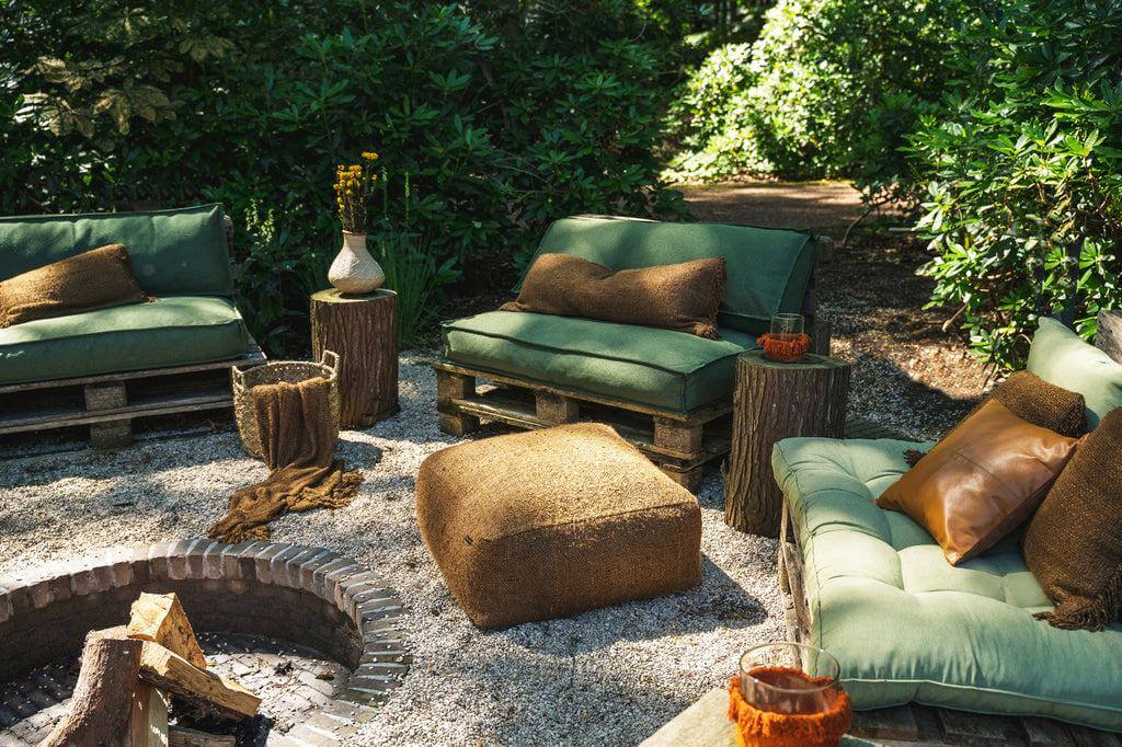 Gezellige boho-tuinopstelling met groene banken, bruine kussenhoezen en natuurlijke houten accenten rond een vuurplaats.
