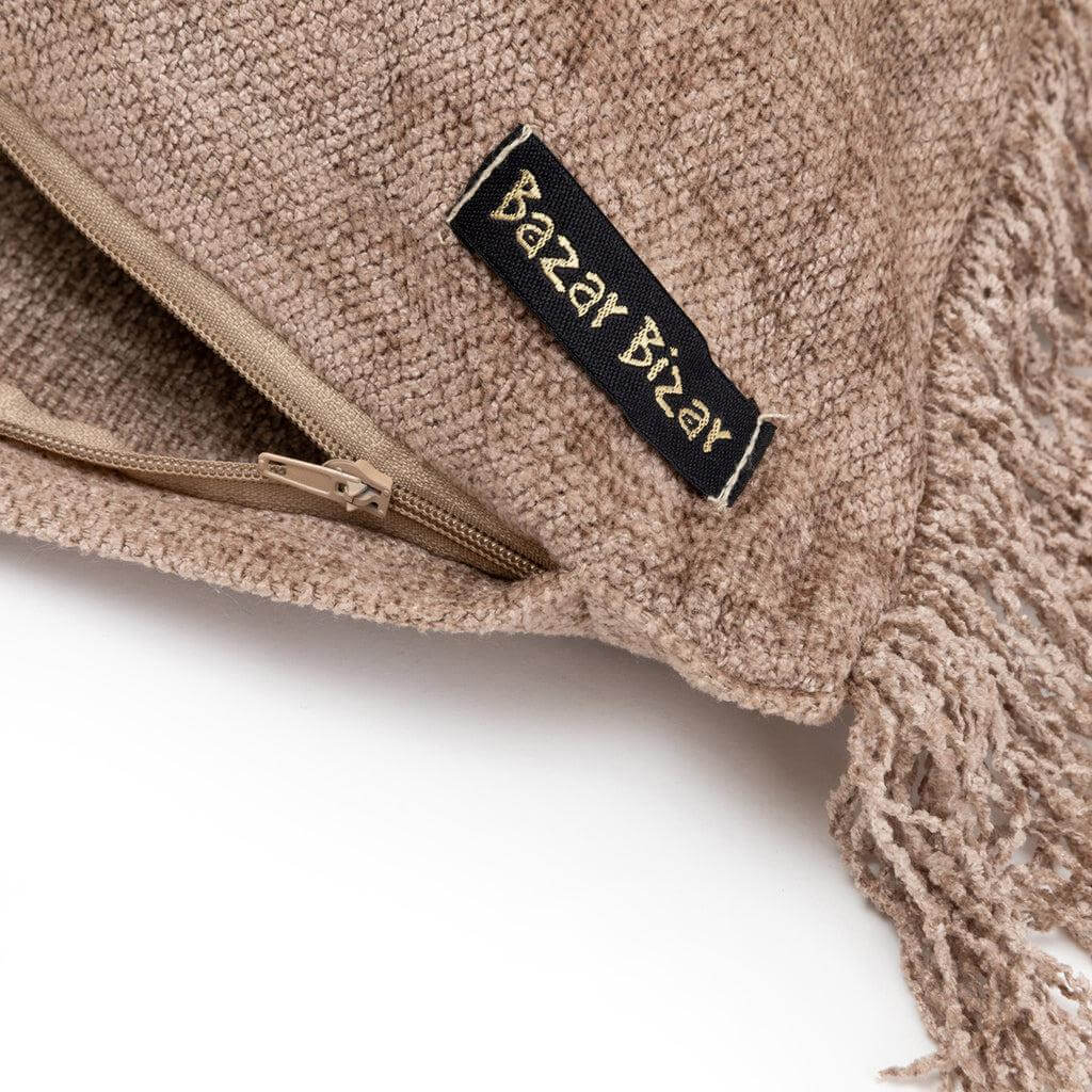 Close-up van een handgemaakte kussenhoes in betonfluweel met kwastjes en rits, label "Bazar Bizar" zichtbaar.